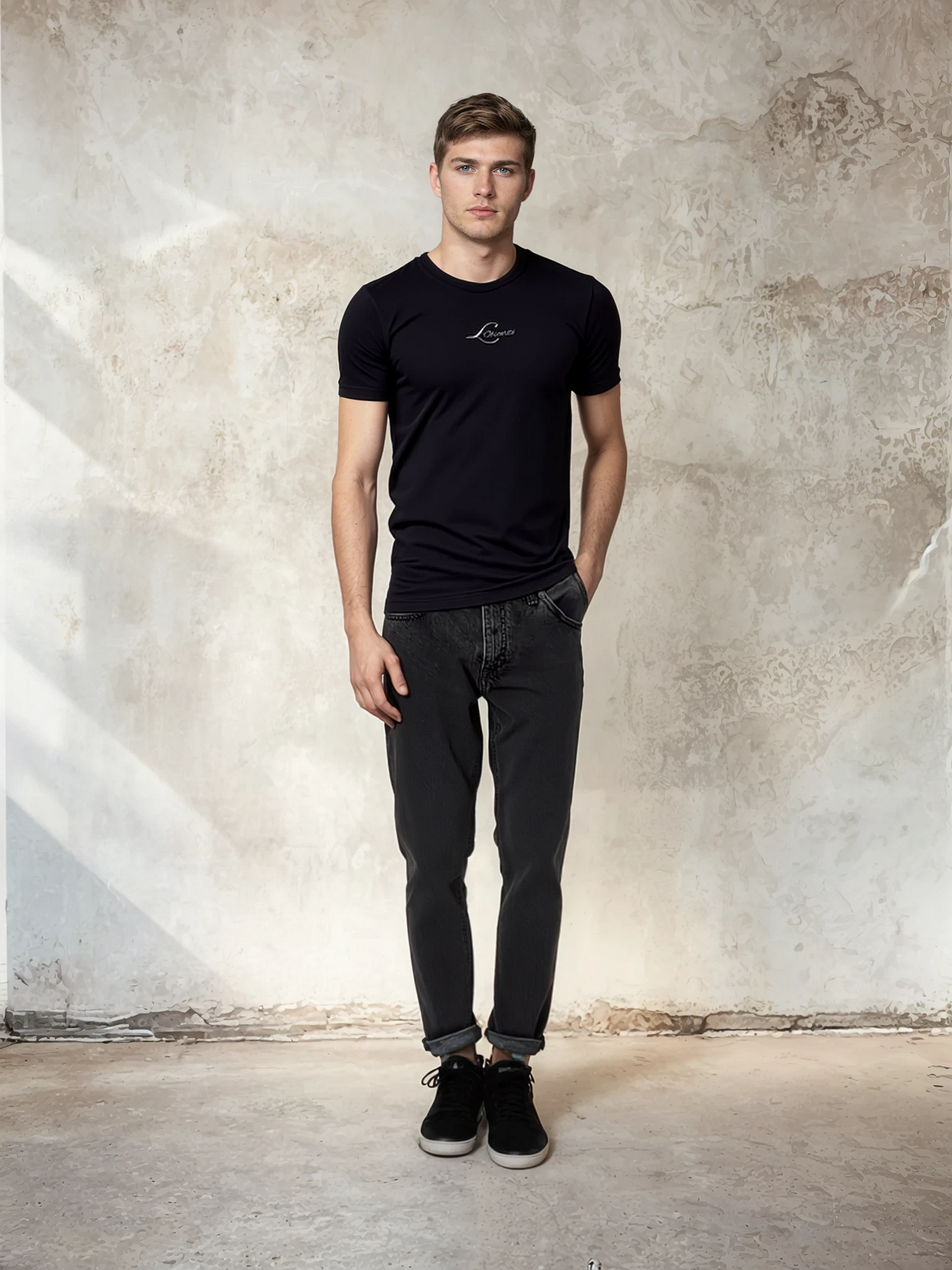 Man wearing a black t-shirt and jeans standing against a textured wall. The mark
