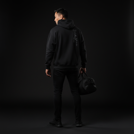 Person wearing a black hoodie and pants holding a black bag against a dark background, black magic hoodie