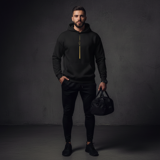 Man wearing a black hoodie and pants holding a black bag against a dark background, essence pullover hoodie