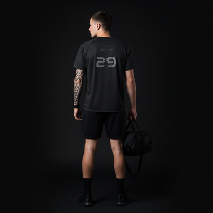 Person wearing a black t-shirt with the number 29 on the back, holding a black bag against a dark background.