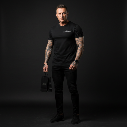 Man wearing a black t-shirt and pants holding a black bag against a dark background, the uniform of silence