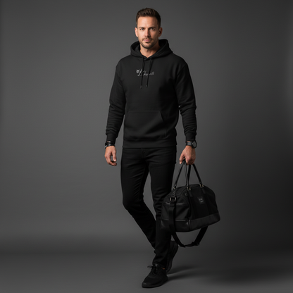 A man wearing a black hoodie and pants holding a black bag on a grey background, serval hoodie