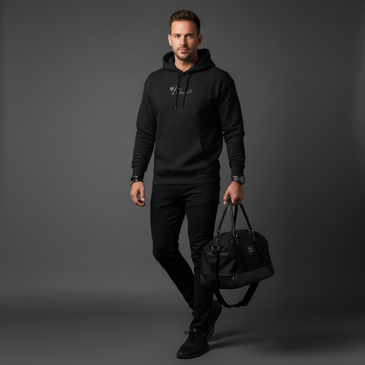 A man wearing a black hoodie and pants holding a black bag on a grey background, serval hoodie