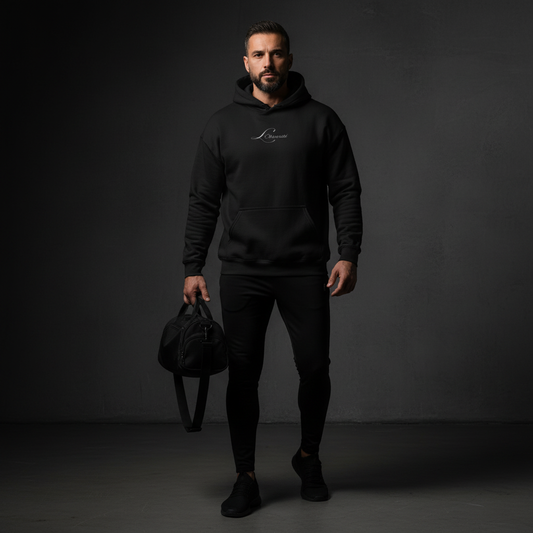 Man wearing a black hoodie with a logo, holding a black bag against a dark background, the mark hoodie